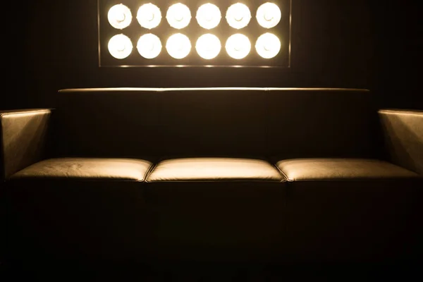 Brown sofa in a dark room. Light falls behind a stand with light bulbs.