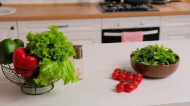 Taze yeşil salata, yeşil ve kırmızı biber ve beyaz mutfak arka planına karşı bir masada vişneli domates..