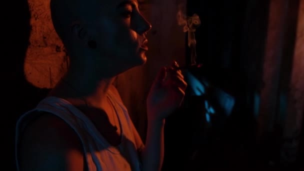 一个秃头女孩的画像 她耳朵里有隧道 还有一个香烟特写 霓虹灯下的空旷房间 那女孩抽烟又抽烟 — 图库视频影像