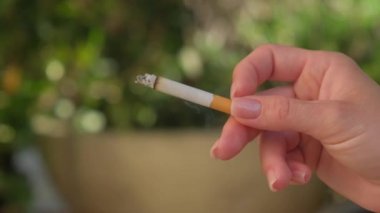 Bir kadının eli sigarayı yakın plan çekimde tutar..