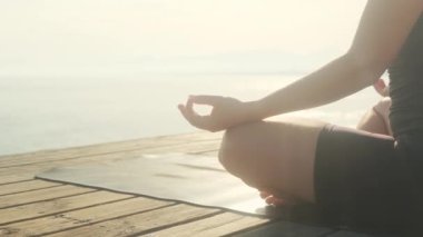 Genç bir kadın bir yaz günü denizin arka planında yoga yapıyor..