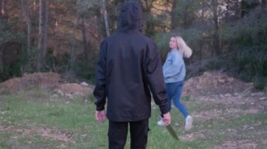 A man with a knife in the forest. The maniac pursues the victim and prepares to attack. The girl runs away from the killer.
