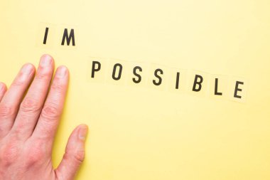 Yazı, sarı arkaplanda olanaksız. İşaret parmağı olan bir erkek eli sözcüğü işaret eder. Yakın plan..