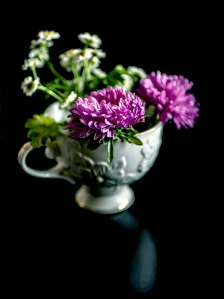 暗い背景のテーブルの上にテーブルの上にカモミールに似た紫色の星と花の美しい小さな花束 狭い焦点領域 柔らかい焦点 — ストック写真