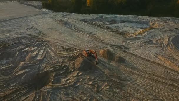 Vykopávač vyrovnává povrch písku na staveništi při západu slunce