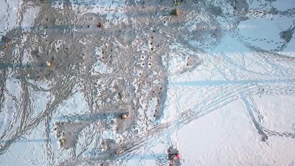Een drone stijgt op tot een hoogte boven een bevroren rivier waar vissers op een winterdag tussen bevroren schepen zitten — Stockvideo