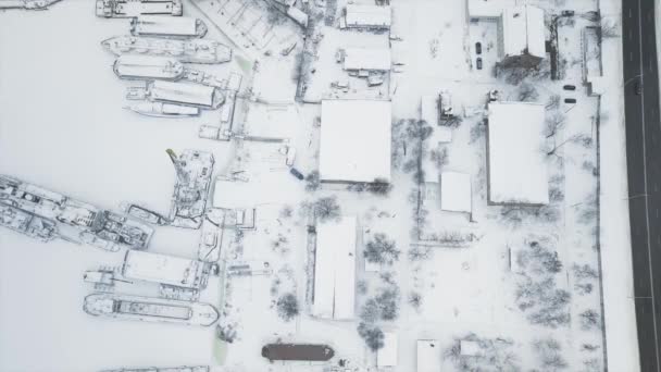 Fliegen auf einer Drohne direkt über der Werft und dem Stand, an dem die Schiffe im Eis eingefroren sind, zur Winterlagerung an einem verschneiten Wintertag — Stockvideo