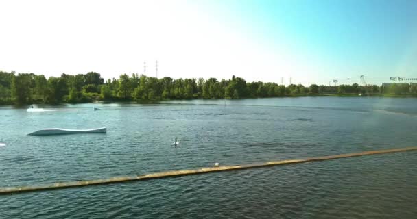 Aerial view of the anchorage of the cable car wake park, and an athlete cutting through the water, on a sunny hot day — Stock Video