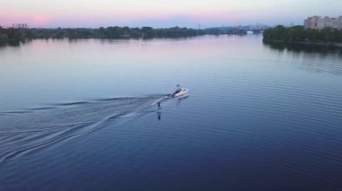 aerial photography, wakeboarding, wakeboarding behind a boat at sunset, top view against the background of the coast and houses. High quality 4k footage