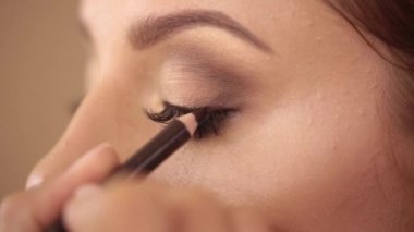 Make-up artist draws a line with a pencil over eyelashes, paints the eye, close-up. High quality footage
