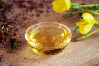 Bir kase çuha çiçeği yağı. Arka planda taze çiçek ve tohum var.