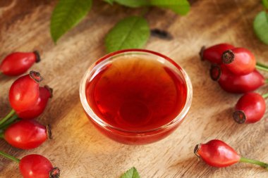 Bir kasede gül tohumu yağı ve masada taze gül kalçası.