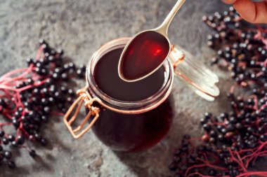 Ev yapımı siyah yaşlı şurubu ile bir kaşık, arka planda taze elderberry ile