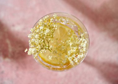 Turunçgilli yaz limonatası ve pembe arka planda taze yaşlı çiçekler.