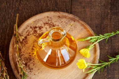 Bir şişe çuha çiçeği yağı. Arka planda taze bitki ve tohumlar var.