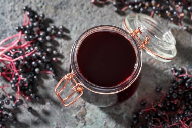 Arka planda freh sambucus meyveleri olan bir kavanoz siyah yaşlı şurubu.