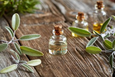 Masada taze adaçayı dalları olan bir şişe aromaterapi.