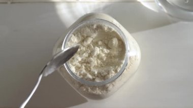 Plastik bir kavanozdan yavaş çekimde beyaz protein tozu alıyor.