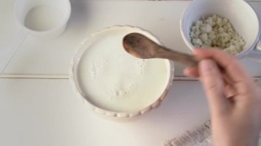 Bir kaşıkla taze süte kefir taneleri koymak - ev yapımı mayalanmış içecek hazırlamak