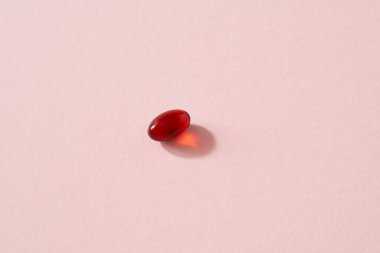 Krill oil pill or softgel on pastel pink background with copy space - nutritional supplement rich in omega-3