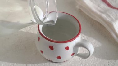 Pouring homemade milk kefir into a cute dotted cup on a table, slow motion
