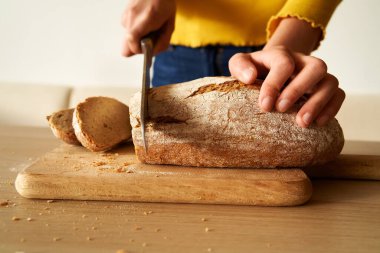 Eller bir somun ev yapımı mayalı ekmeği bıçakla kesiyor.