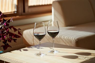 Güneşli bir dairede masada iki kadeh kırmızı şarap.