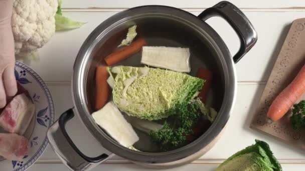 手は水と新鮮な野菜と鍋に牛の骨髄の骨を入れて 自家製のスープやスープの準備 — ストック動画