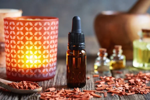 A dropper bottle of aromatherapy essential oil with red sandalwood pieces and a candle