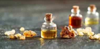 Şeffaf bir aromaterapi şişesi. Esmer arka planda tütsü reçinesi kristalleri olan gerekli yağ.