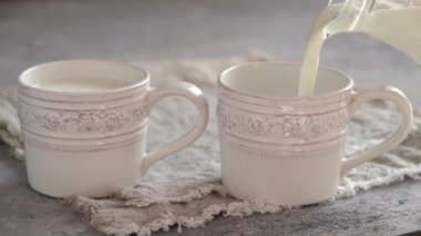 İki beyaz fincana ev yapımı kefir dökülüyor, ağır çekimde.