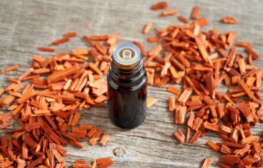 Masasında kırmızı sandal ağacı parçaları olan koyu bir yağ şişesi.