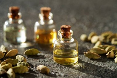 Aromaterapi şişeleri koyu arkaplanda kakule tohumlarıyla gerekli yağ.