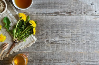Wooden background with fresh dandelion flowers with root, honey and herbal tea