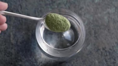 Bir bardak suya yeşil arpa tozu dökmek - sağlıklı bir içecek hazırlamak