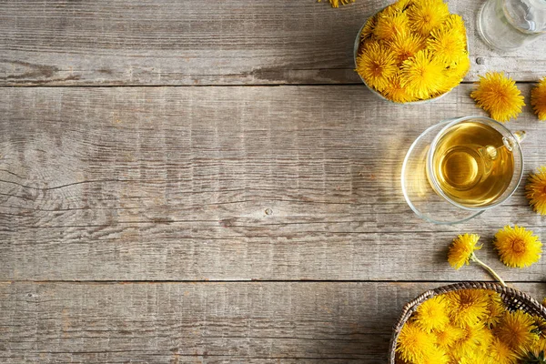 Tahta arka plan, taze karahindiba çiçekleri ve ilkbaharda bir fincan bitki çayı.