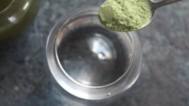 Pouring green barley grass powder into a glass of water, top view