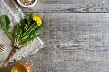 Kurumuş kökleri olan taze karahindiba çiçekleri ve kopyalanmış arkaplanda bir kavanoz bal.