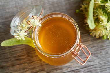 A glass jar of honey with fresh linden flowers on a table in spring