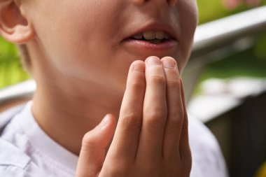 Fingers of a little boy practicing EFT or emotional freedom technique outdoors - tapping on the chin point