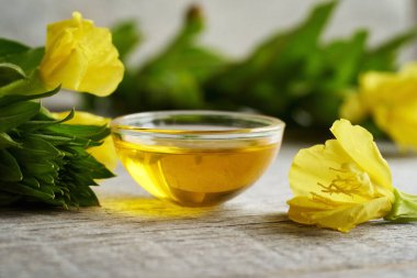 Evening primrose oil in a bowl with fresh blooming Oenothera biennis plant on a table