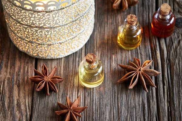 A transparent bottle of essential oil with star anise and an aromalamp on rustic background