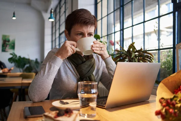 Woman sitting in a cafe with a laptop, drinking coffee. Remote working or learning.