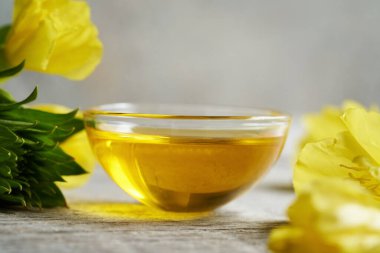 Evening primrose oil in a bowl with fresh Oenothera biennis flowers on a table