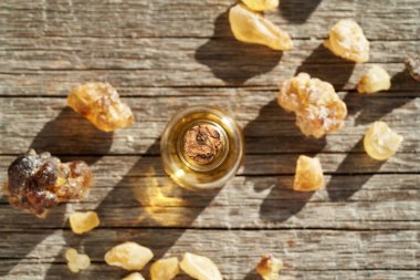 A bottle of frankincense essential oil with boswellia resin on a wooden table, top view