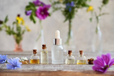 Bottles of aromatherapy essential oils with frankincense resin, herbs and summer flowers