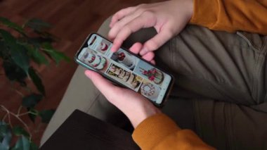 Bir genç elinde akıllı bir telefon tutuyor, pasta resimlerine bakıyor ve tatil için bir pasta tasarımı seçiyor..