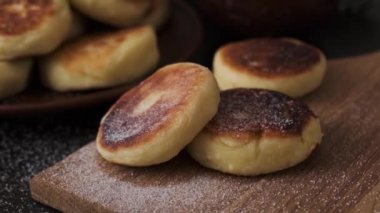 Süzme peynirden yapılmış peynirli kekler ahşap bir tahtada, çömlekçilikte, karanlık bir masada. Ev yapımı süzme peynirli hamur işleri. Tüm aile için protein kahvaltısı..