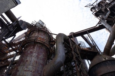 Aşağıdan görülen endüstriyel bir tesiste paslanmış metal yapılar, çeşitli şekil ve dokular, yatay görünüm