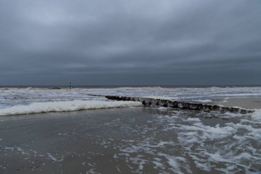 Karanlık gökyüzü ve deniz köpüğünün bol olduğu dalgalı dalgalar metal erozyon kontrol duvarı boyunca, Güney Carolina kıyıları, yatay görünüm